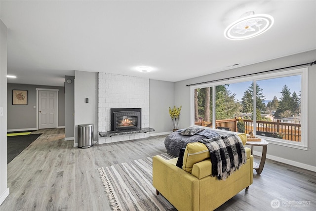 living area with a brick fireplace, baseboards, and wood finished floors