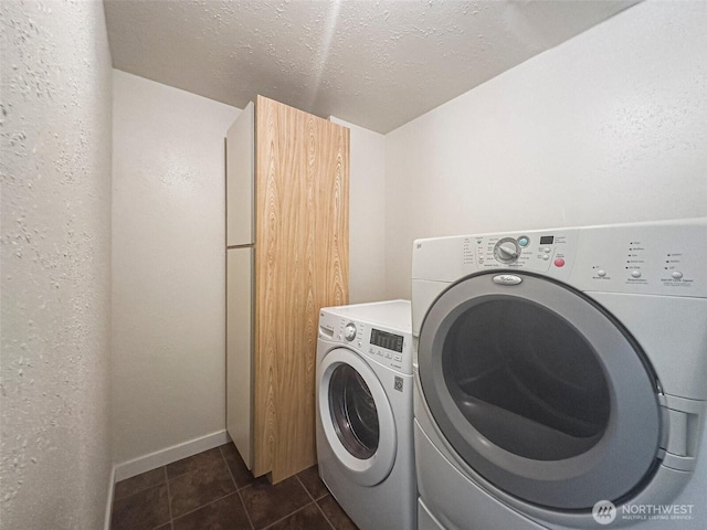 washroom with a textured ceiling, a textured wall, washing machine and dryer, dark tile patterned floors, and baseboards