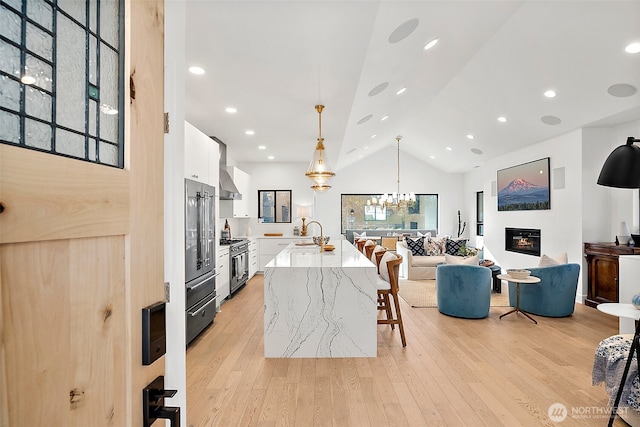 kitchen with a breakfast bar, high end appliances, hanging light fixtures, white cabinetry, and an island with sink