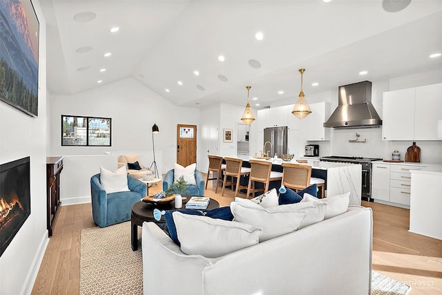 living room with lofted ceiling, a glass covered fireplace, light wood-style flooring, and recessed lighting