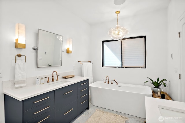 full bath featuring a chandelier, a freestanding tub, vanity, and marble finish floor