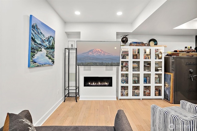 living area with a warm lit fireplace, recessed lighting, wood finished floors, and baseboards