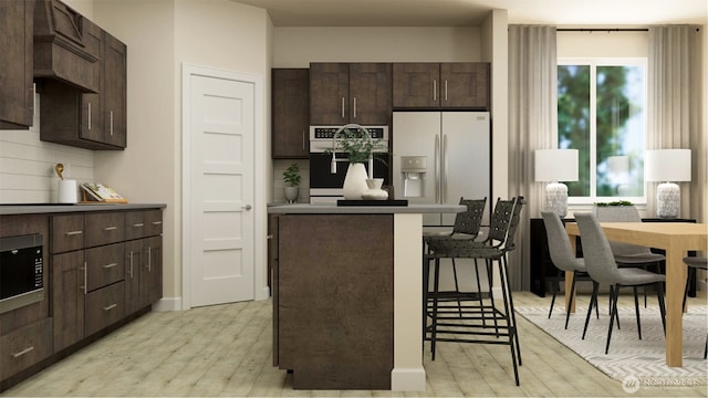 kitchen with light hardwood / wood-style floors, backsplash, dark brown cabinets, appliances with stainless steel finishes, and a breakfast bar area