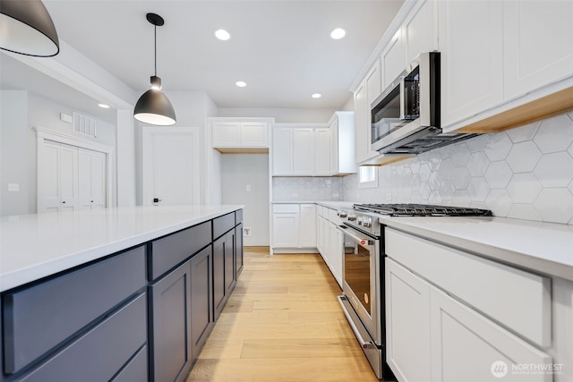 kitchen featuring pendant lighting, light wood finished floors, light countertops, appliances with stainless steel finishes, and white cabinetry