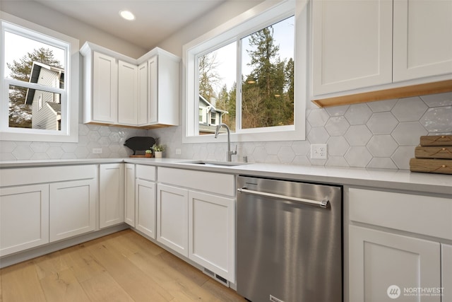 kitchen with a sink, white cabinetry, light countertops, stainless steel dishwasher, and light wood finished floors