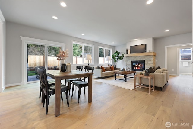 dining area with a wealth of natural light, a stone fireplace, light wood-style flooring, and recessed lighting