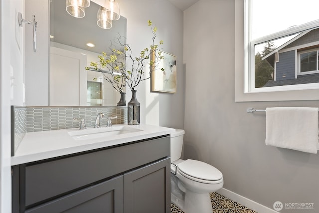 bathroom with baseboards, toilet, vanity, and decorative backsplash