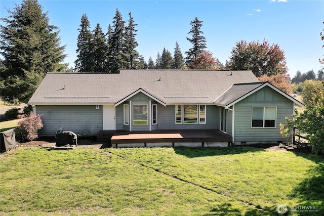 back of house featuring a deck, a shingled roof, a lawn, and board and batten siding