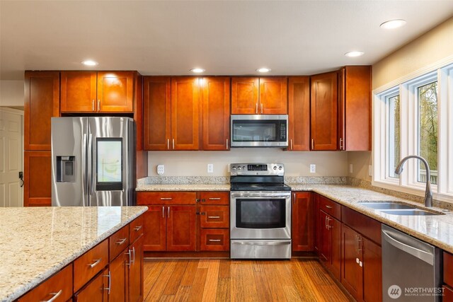 kitchen with recessed lighting, a sink, light wood-style floors, appliances with stainless steel finishes, and light stone countertops