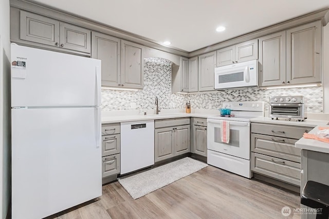 kitchen with white appliances, light hardwood / wood-style floors, sink, and decorative backsplash