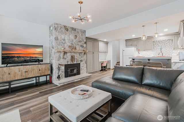 living room with sink, a stone fireplace, dark hardwood / wood-style floors, and an inviting chandelier