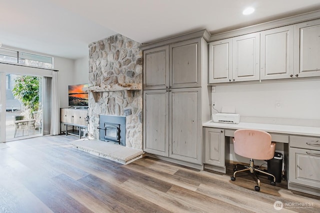 office space with light hardwood / wood-style flooring, built in desk, and a wood stove