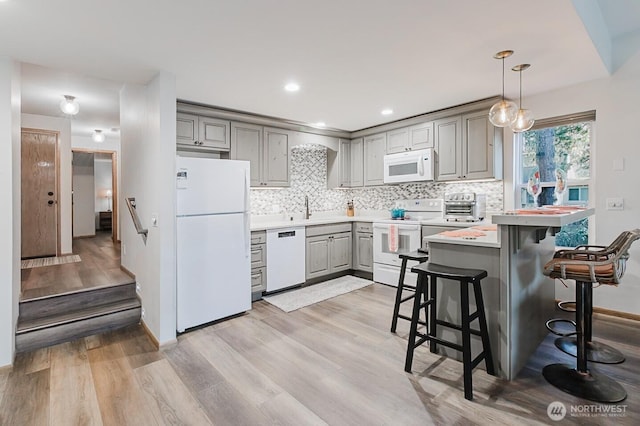 kitchen featuring white appliances, pendant lighting, gray cabinetry, and a breakfast bar area