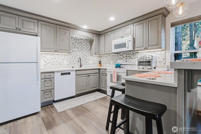 kitchen featuring a kitchen breakfast bar, white appliances, light wood-type flooring, decorative backsplash, and sink