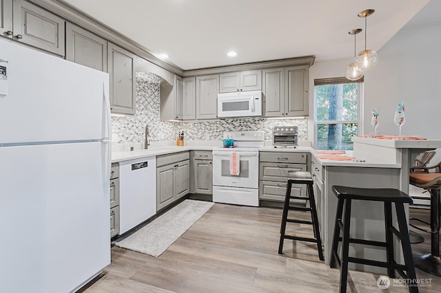 kitchen with white appliances, tasteful backsplash, a breakfast bar, and light wood-type flooring