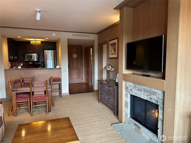 living room with ornamental molding, a tiled fireplace, visible vents, and light colored carpet