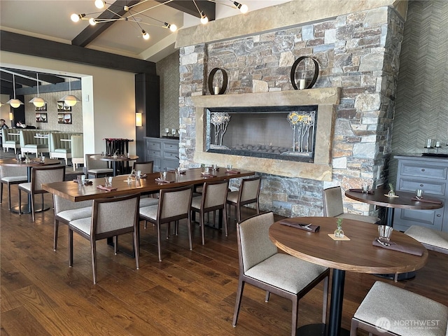 dining space featuring lofted ceiling with beams, an inviting chandelier, a fireplace, and wood finished floors