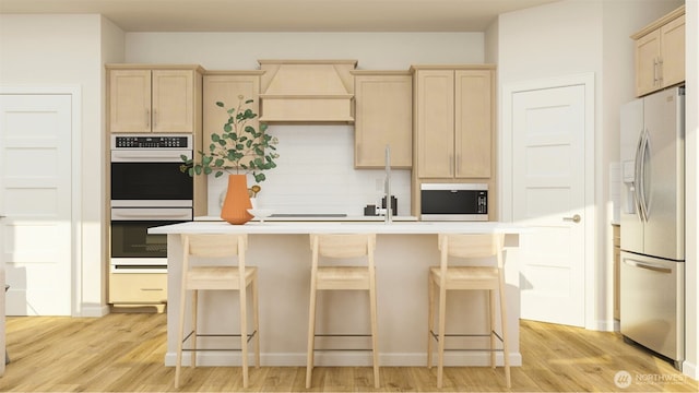 kitchen featuring an island with sink, stainless steel appliances, a breakfast bar, custom exhaust hood, and light brown cabinetry