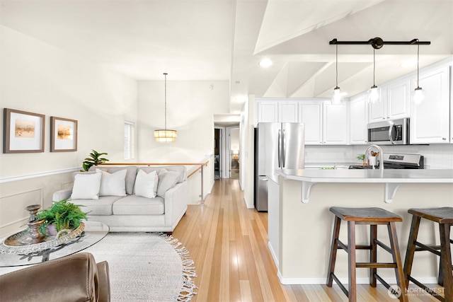 kitchen with a breakfast bar, light wood finished floors, decorative backsplash, appliances with stainless steel finishes, and white cabinets