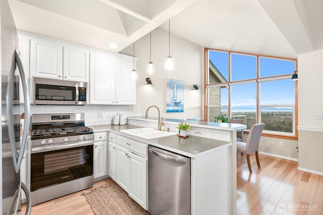 kitchen with stainless steel appliances, a peninsula, a sink, white cabinets, and light wood finished floors