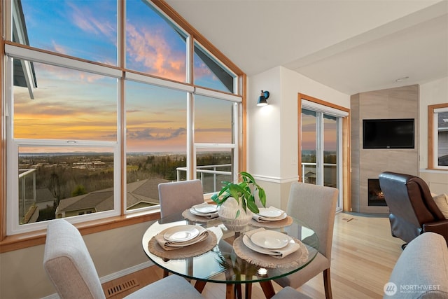 dining space featuring baseboards, visible vents, a tile fireplace, lofted ceiling, and wood finished floors