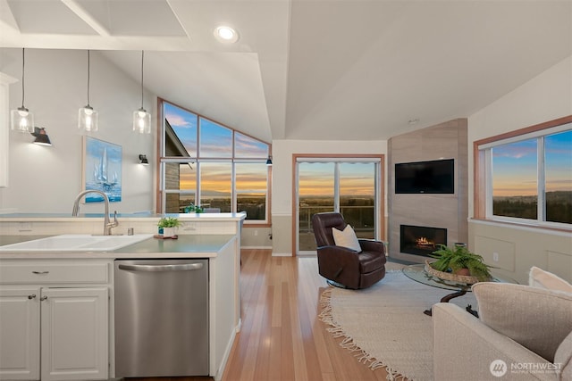 kitchen with a large fireplace, vaulted ceiling, open floor plan, and stainless steel dishwasher