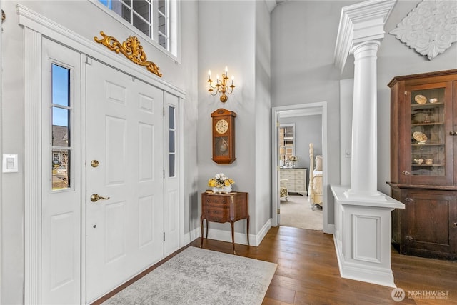 foyer entrance with baseboards, dark wood-type flooring, a towering ceiling, and ornate columns