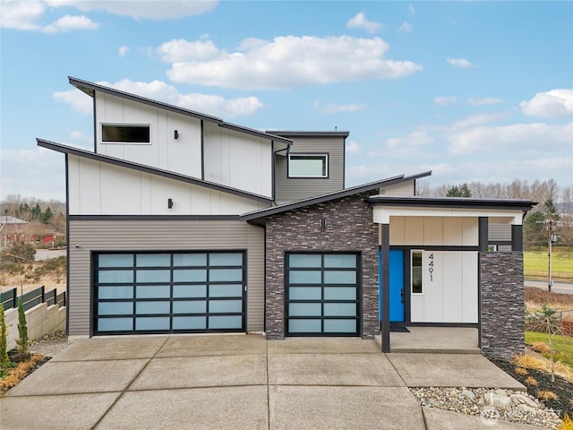 modern home with board and batten siding, stone siding, fence, and concrete driveway