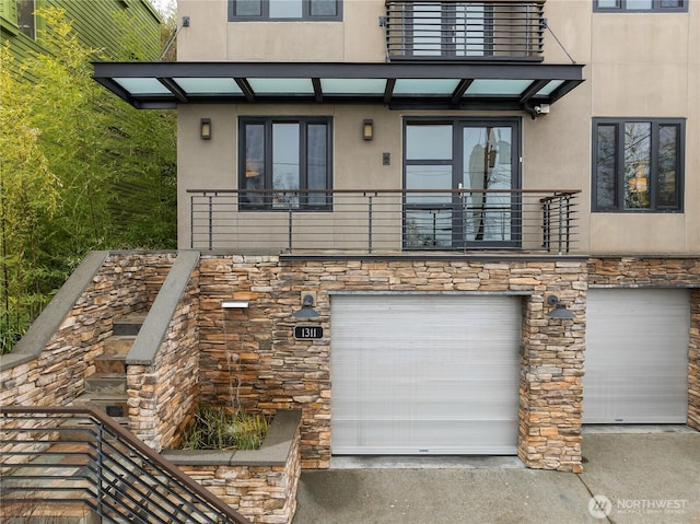 view of front of property featuring stone siding, driveway, a balcony, and stucco siding