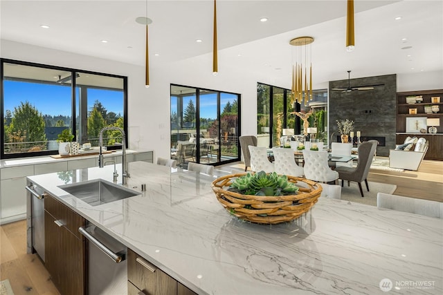 kitchen featuring light hardwood / wood-style flooring, sink, pendant lighting, dark brown cabinetry, and light stone countertops