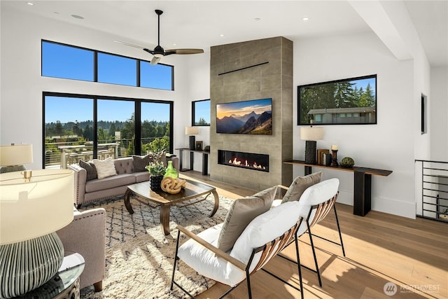 living room featuring a fireplace, ceiling fan, a high ceiling, and light hardwood / wood-style floors