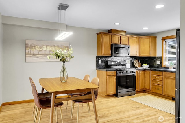 kitchen with hanging light fixtures, appliances with stainless steel finishes, decorative backsplash, brown cabinetry, and dark countertops