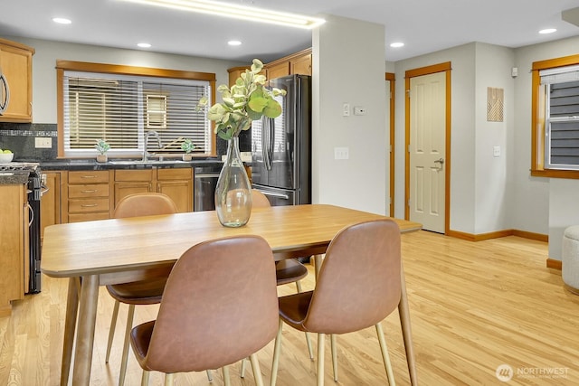 kitchen featuring stainless steel appliances, a sink, light wood-style floors, light brown cabinetry, and dark countertops