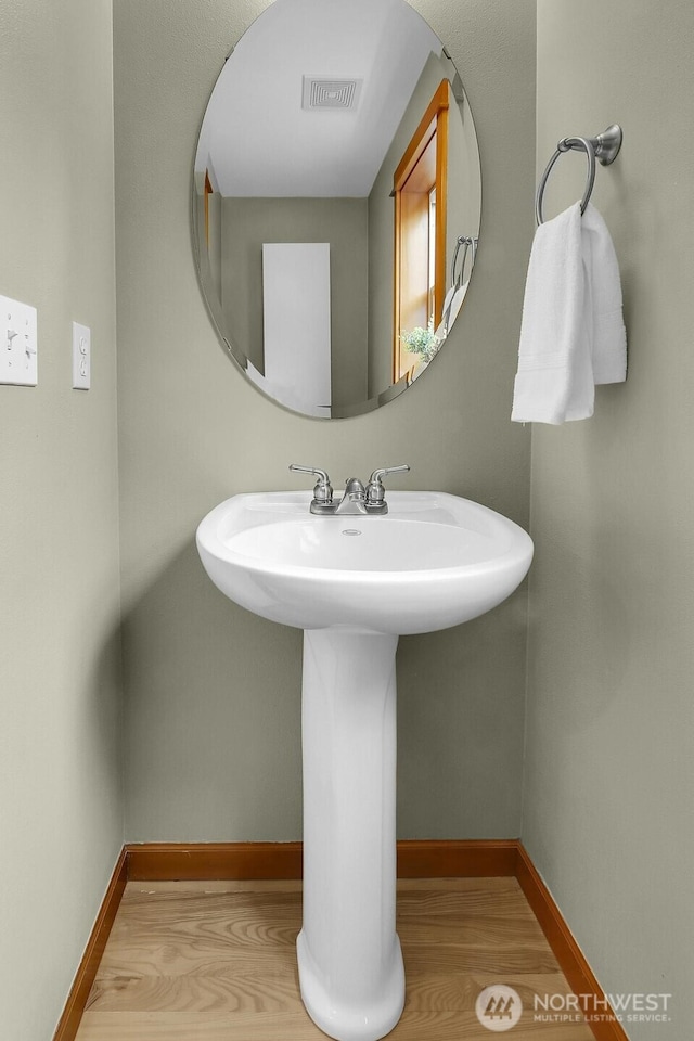 bathroom featuring visible vents, a sink, baseboards, and wood finished floors