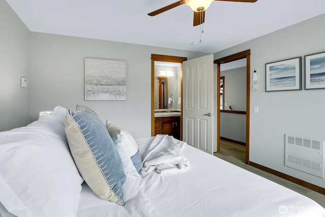 bedroom featuring baseboards, ensuite bath, ceiling fan, wood finished floors, and a sink