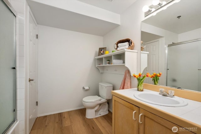 bathroom with toilet, vanity, hardwood / wood-style floors, and a shower with door