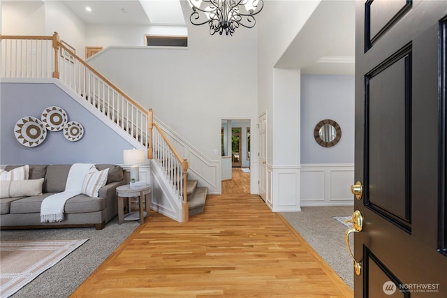 entrance foyer featuring a wainscoted wall, an inviting chandelier, carpet, a decorative wall, and stairs