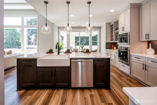 kitchen with sink, light hardwood / wood-style floors, stainless steel appliances, hanging light fixtures, and tasteful backsplash