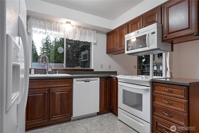 kitchen featuring dark countertops, white appliances, and a sink