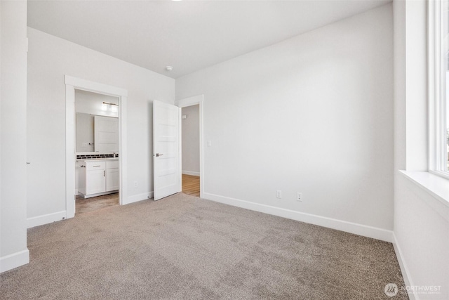 unfurnished bedroom featuring light colored carpet, connected bathroom, and baseboards