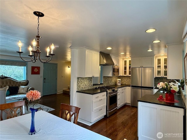 kitchen featuring wall chimney range hood, pendant lighting, stainless steel appliances, and white cabinets