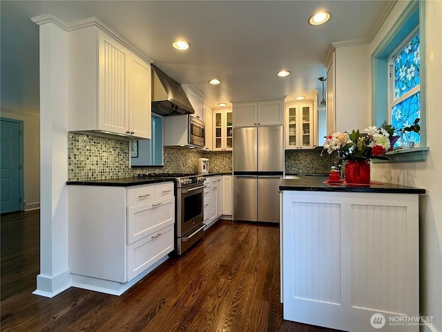 kitchen featuring appliances with stainless steel finishes, tasteful backsplash, dark wood-type flooring, wall chimney exhaust hood, and white cabinets