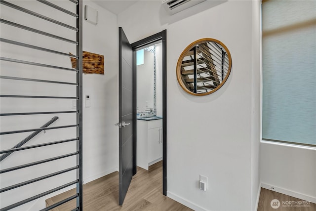 hallway with an AC wall unit, light wood-type flooring, and baseboards