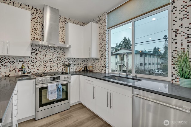 kitchen with appliances with stainless steel finishes, dark countertops, white cabinetry, and wall chimney range hood