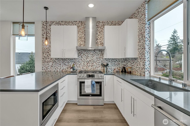 kitchen with pendant lighting, appliances with stainless steel finishes, white cabinetry, a sink, and wall chimney range hood