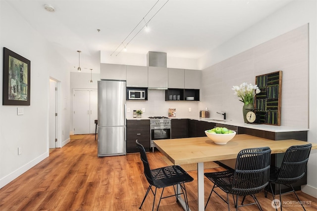 kitchen with a sink, light countertops, appliances with stainless steel finishes, wall chimney range hood, and light wood finished floors