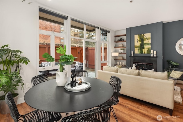 dining area featuring expansive windows, a glass covered fireplace, wood finished floors, and baseboards