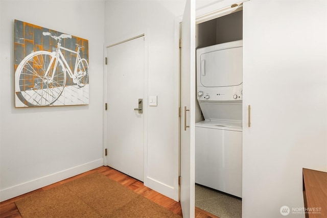 laundry room featuring stacked washer / dryer, laundry area, baseboards, and wood finished floors