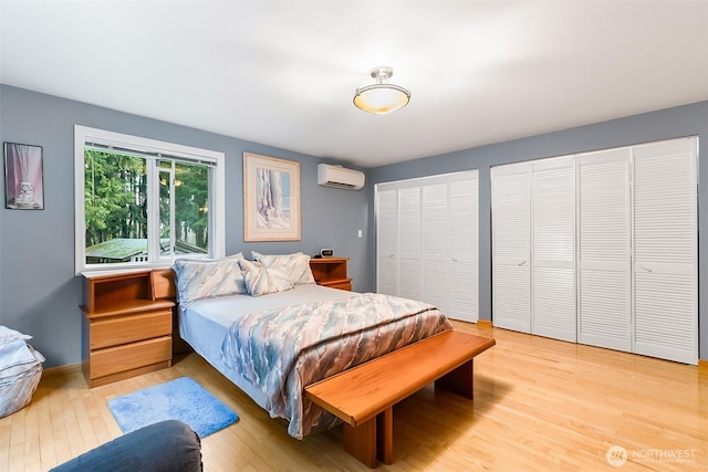 bedroom with light hardwood / wood-style floors, a wall mounted AC, and two closets