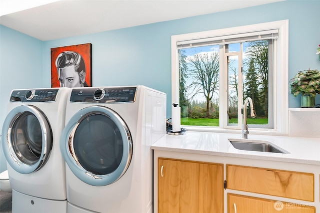 clothes washing area featuring washing machine and clothes dryer, sink, and cabinets